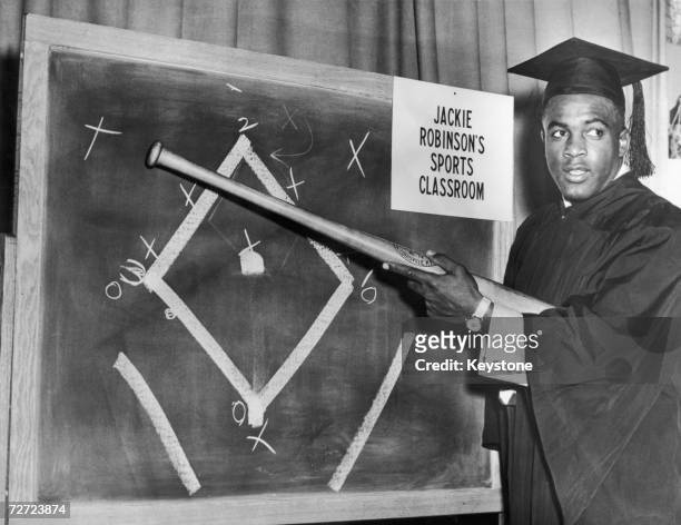 Brooklyn Dodger Jackie Robinson wearing a teachers outfit and mortarboard while illustrating baseball tactics on a blackboard in preparation for his...