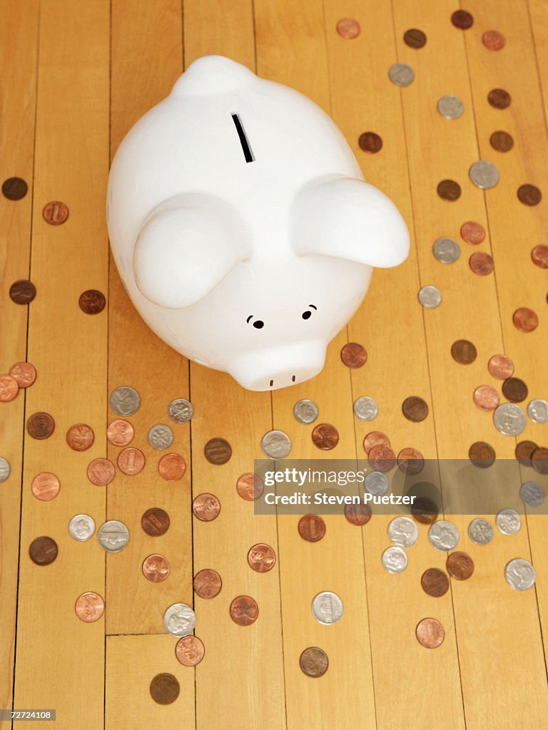 Piggy bank on hardwood floor among coins, elevated view