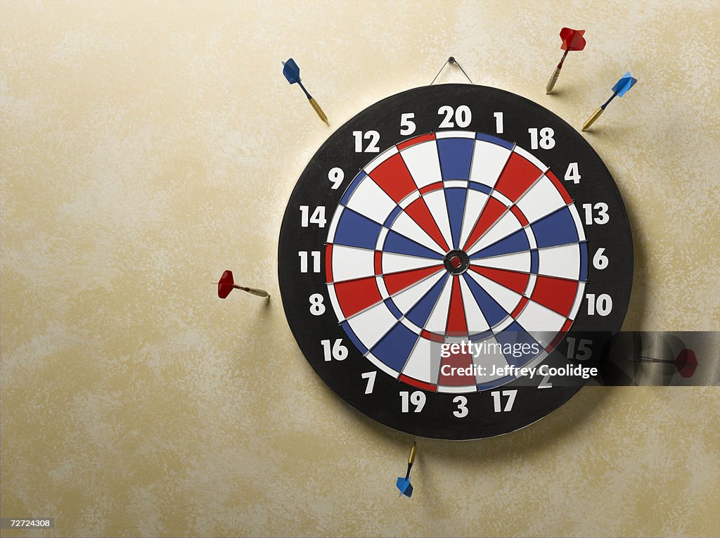 Red and blue darts in wall around red, white and blue dart board