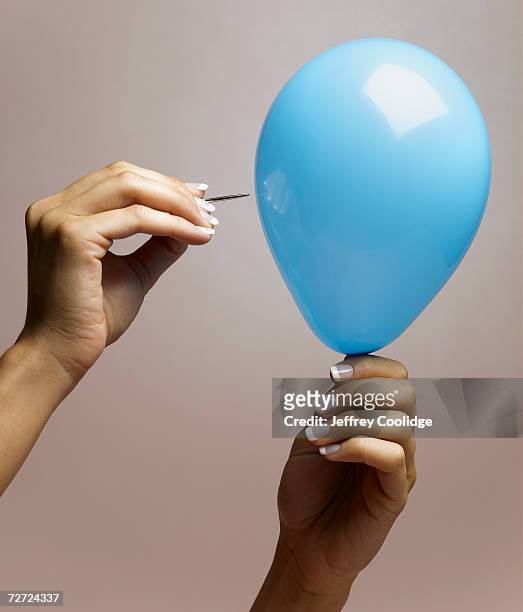 young woman bursting balloon with pin, close up of hands - balloon burst stock pictures, royalty-free photos & images