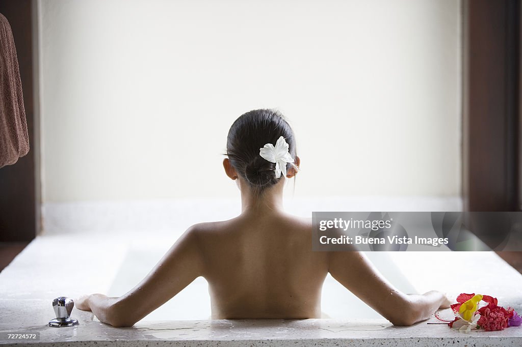 Young woman bathing in large tub with a singe flower hair, rear view