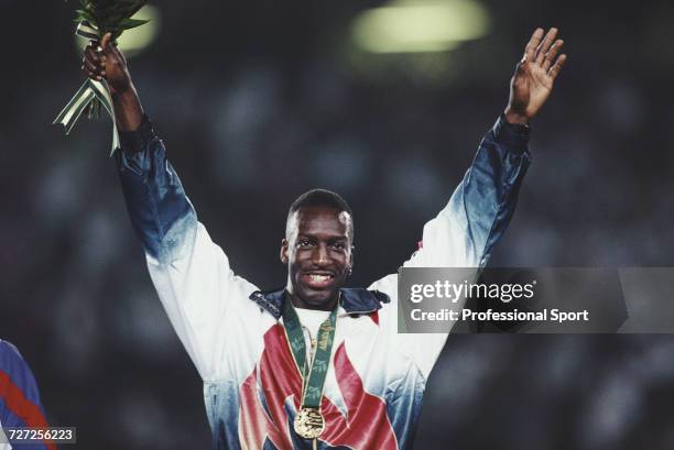 American athlete Michael Johnson raises his arms in the air in celebration on the medal podium after finishing in first place with an Olympic record...