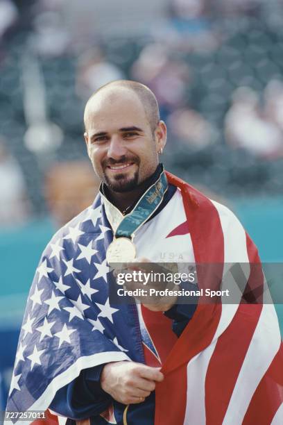 American tennis player Andre Agassi, wrapped in the stars and stripes flag, holds up his gold medal on the podium after winning the final of the...