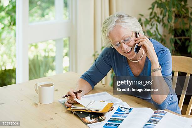woman booking a holiday on cell phone - travel brochure stock pictures, royalty-free photos & images
