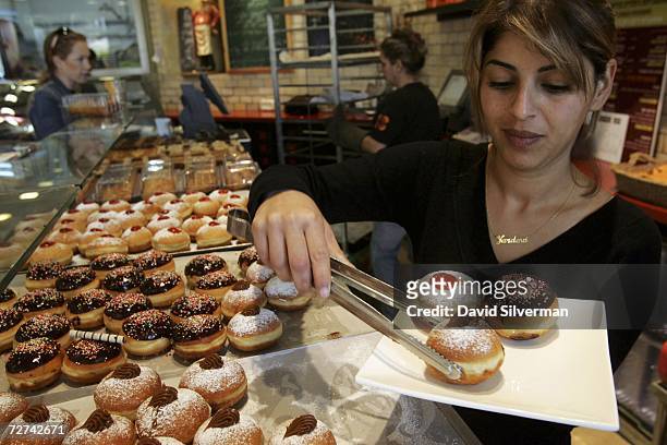 Israeli waitress Yardena Edri prepares a serving of fresh oil-fried and jam-filled doughnuts, called sufganiyot in Hebrew, at the Roladin bakery...