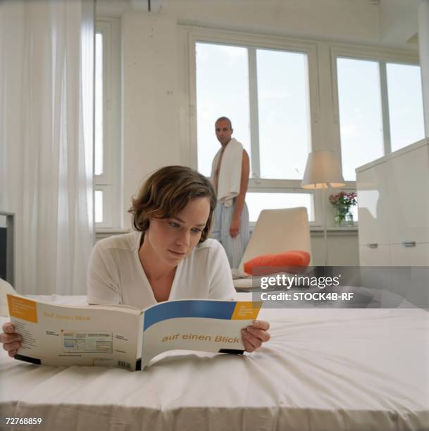 young woman lying in bed while reading a handbook about computers - couple lying in bed and reading a book stock pictures, royalty-free photos & images