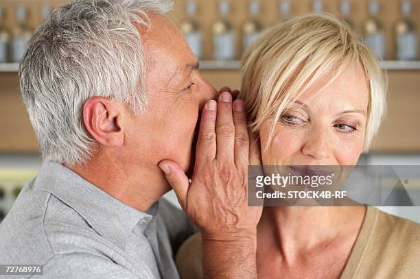 gray-haired man whispering something into the ear of a woman, close-up - ear close up women stock-fotos und bilder