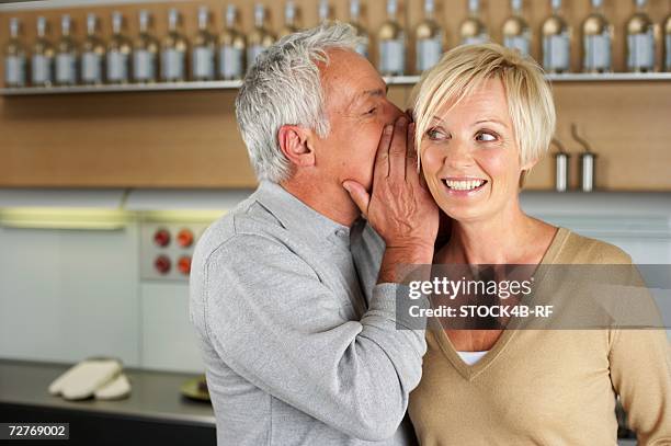 gray-haired man whispering something into the ear of a woman, close-up - ear close up women stock-fotos und bilder