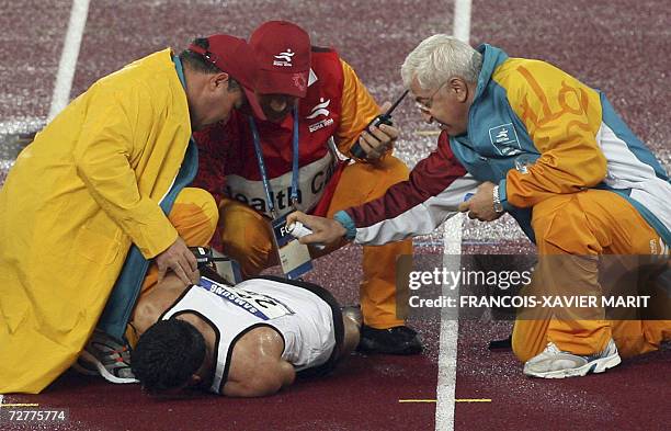 Track officials check on the status of Iraq's Hareth Saleh after he fell in the men's 100m heat 4 on the opening day of the athletics competition for...