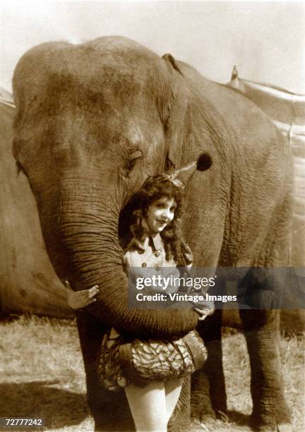 Portrait of American actress Madge Bellamy as she poses in costume with Oscar the Elephant, one of her co-stars in the circus-themed film 'Soul of...