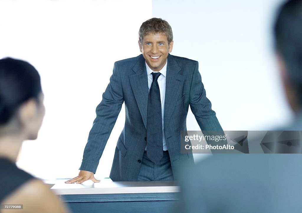 Businessman standing with hands on table, facing colleagues, smiling