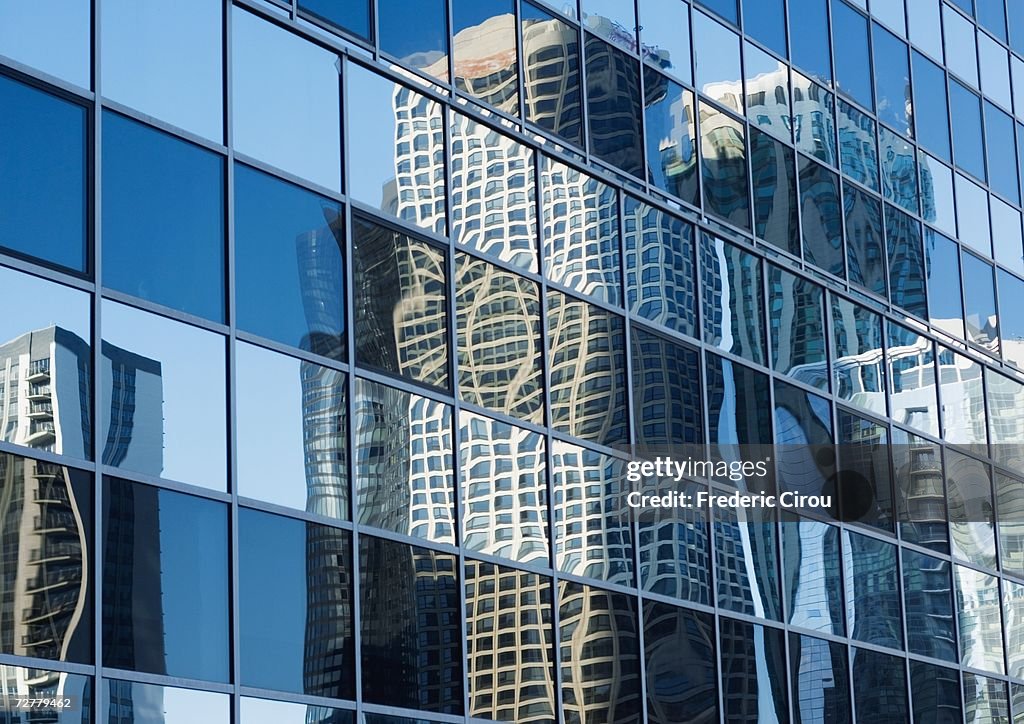 Skyscrapers reflected on glass facade, low angle view