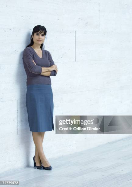 businesswoman standing, leaning against wall, full length - pies cruzados en los tobillos fotografías e imágenes de stock
