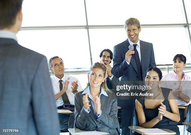 executives in seminar, one man holding microphone, others clapping - microphone debate stock pictures, royalty-free photos & images