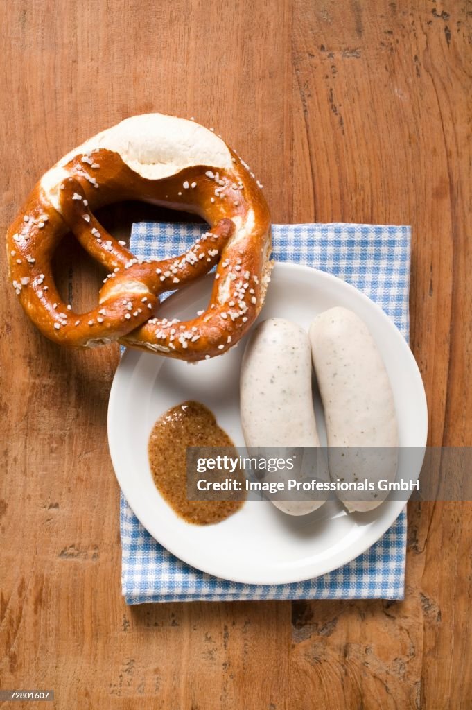 Two cooked Weisswurst with mustard & pretzel on plate