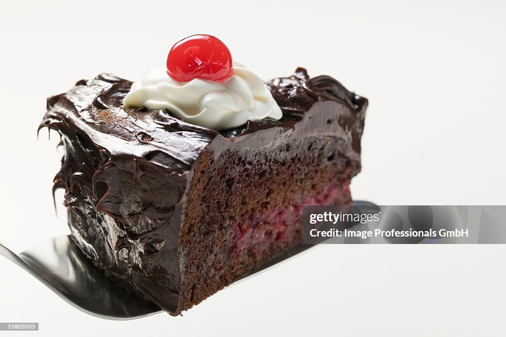 Slice of chocolate cake with cream & cherry on cake server