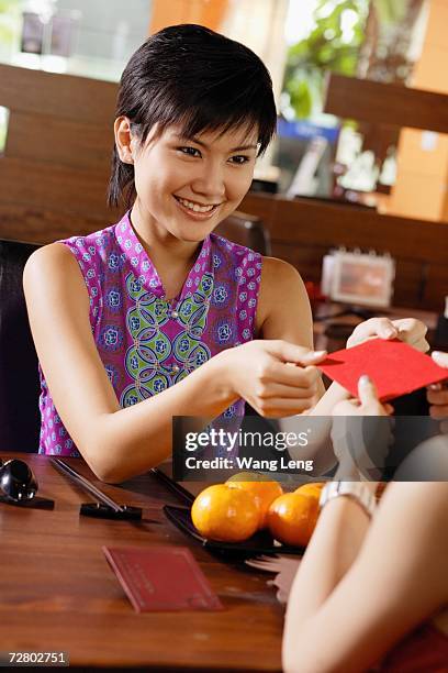 young woman passing a red packet to person facing her - mad about heritage festival stockfoto's en -beelden