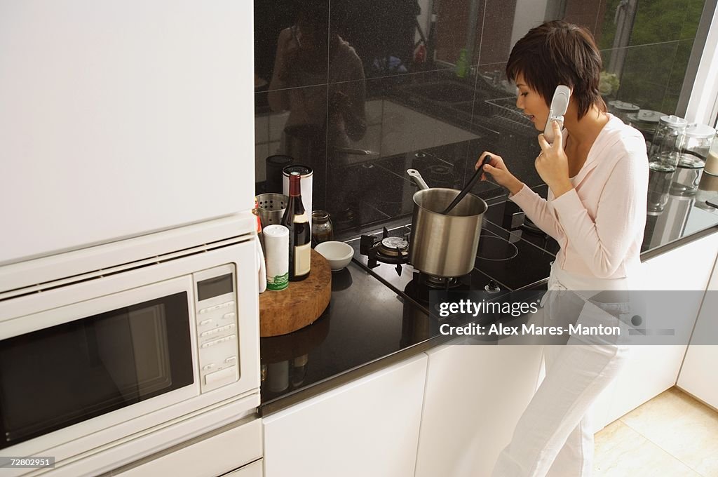 Young woman cooking in kitchen, using mobile phone