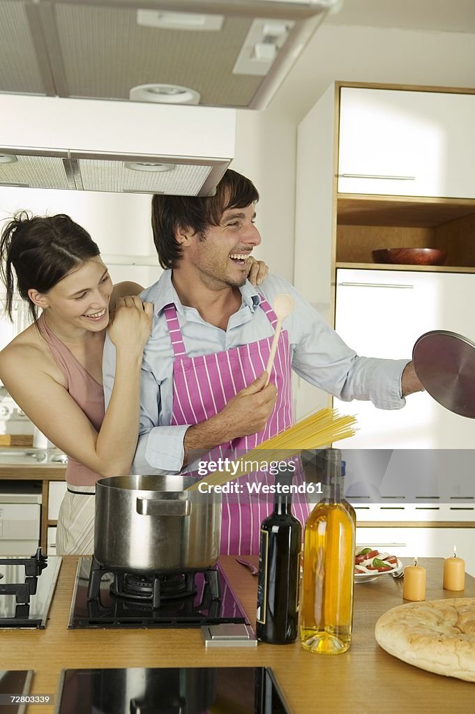 Young couple cooking spaghetti, looking away, smiling