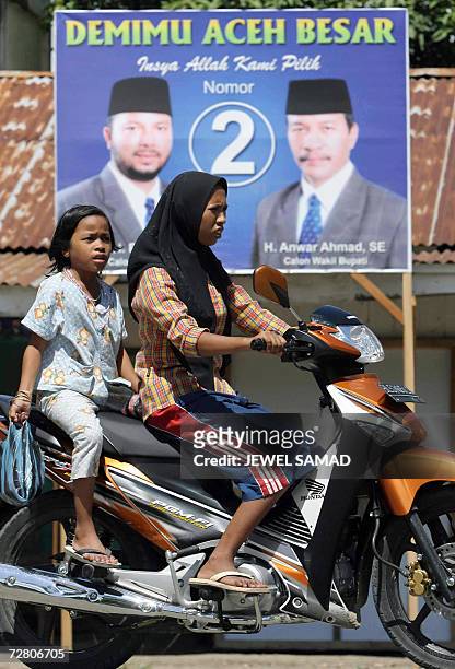 Woman with her daugther ride a motorbike past an election poster in Aceh Besar, 10 December 2006, a day before the provincial election. The...