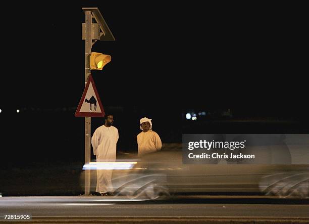 Two men wait next to a camel crossing sign as cars drive pass in Nad Al Sheba on December 13, 2006 in Dubai, United Arab Emirates.