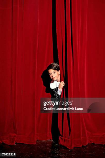 boy (6-7) looking from behind theatre curtain - children theater stock pictures, royalty-free photos & images