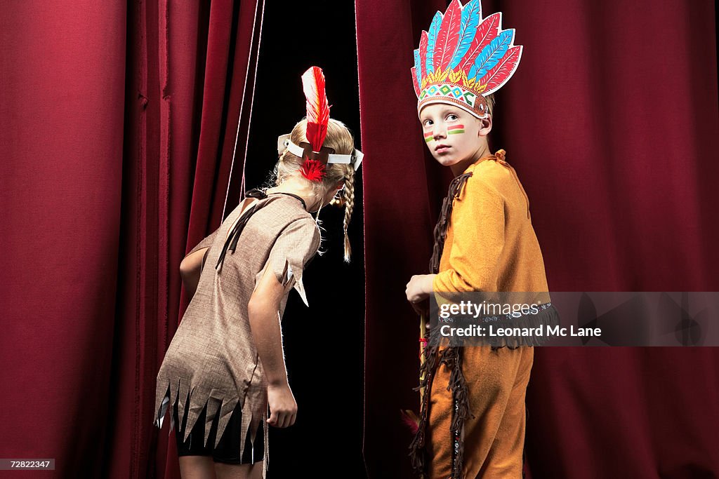 Two children (7-8)  in indian costumes standing between curtains