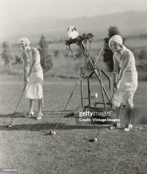 American actress Penny Singleton and another actress take lessons on their golf swings from a mechanical instructor in a scene from the musical...