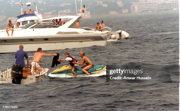 Diana, Princess of Wales, wearing a animal print, halterneck swimsuit and sunglasses, rides on a jet ski with Prince Harry on July 17, 1997 in...