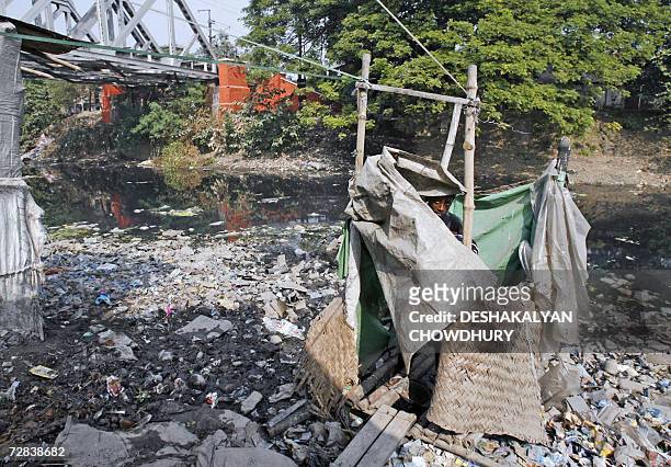 An Indian slum dweller peers out of a makeshift latrine on the edge of a slum colony in Kolkata, 17 December 2006. The Asian Development Bank has...