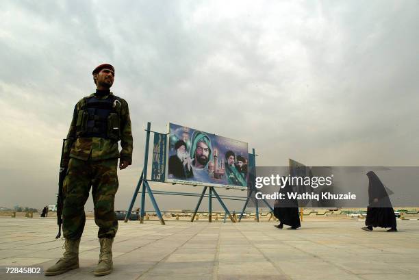Iraqi woman and a solider are seen near a picture that shows Ayatollah Muhammad al-Sad, Imam Hussein, Muhammad Baqir al-Sadr and Moqtada al-Sadr on...
