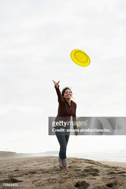 young woman throwing frisbee on beach - throwing frisbee stock pictures, royalty-free photos & images