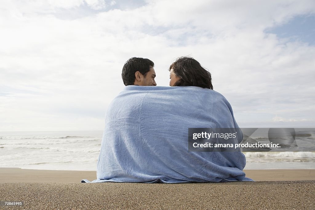 Young couple wrapped in towel on beach (rear view)