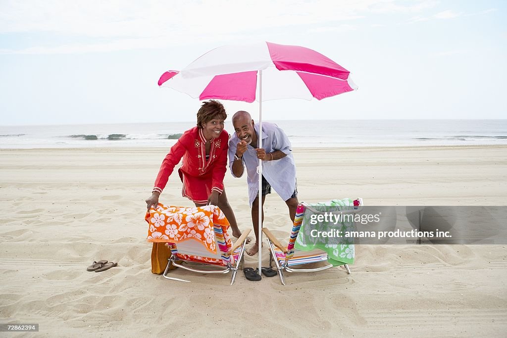 Couple pointing and laughing under beach umbrella