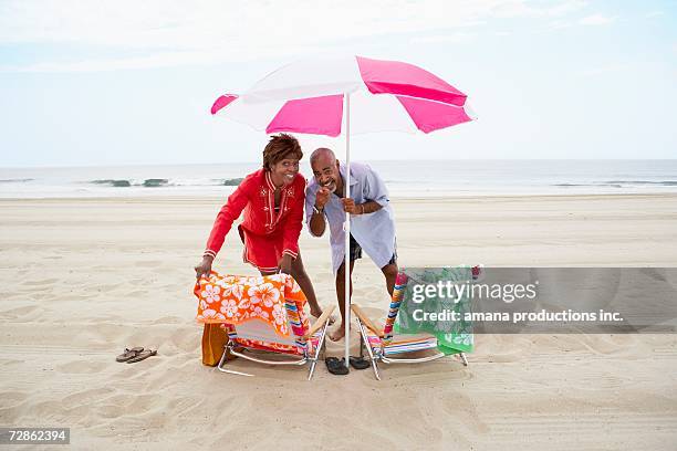 Couple Pointing And Laughing Under Beach Umbrella High-Res Stock Photo