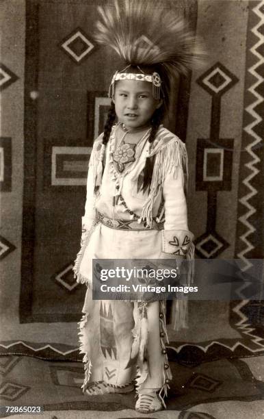 Portrait of young Native American Calvin Last Star as he poses in traditional clothing complete with a tall headdress, Browning, Montana, late 1930s.