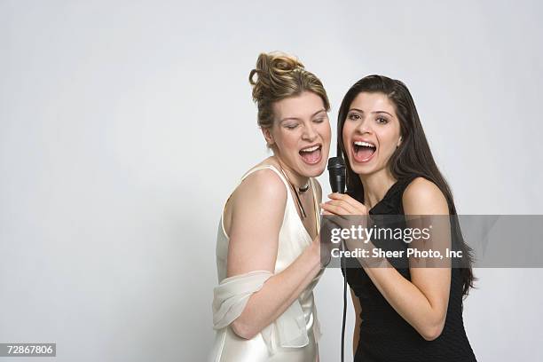 two young women singing into microphone, mouth open, close-up - friends with white background stock pictures, royalty-free photos & images
