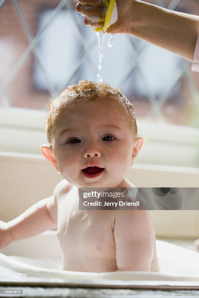 Baby girl (6-9 months) taking a bath in kitchen sink, portrait