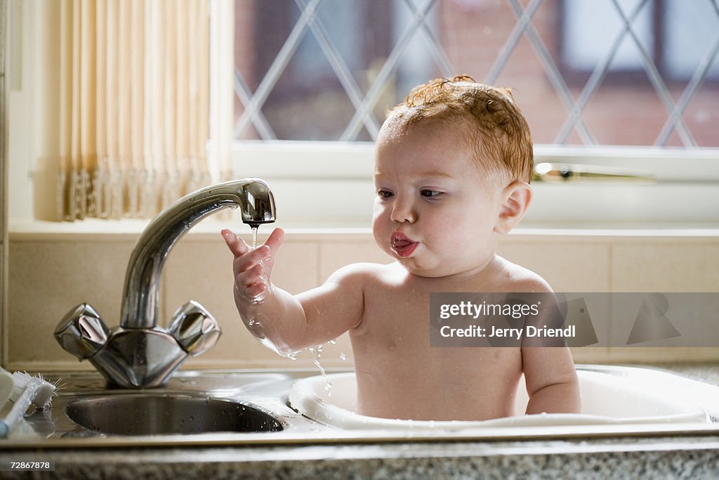 Baby girl (6-9 months) taking a bath in kitchen sink, close-up