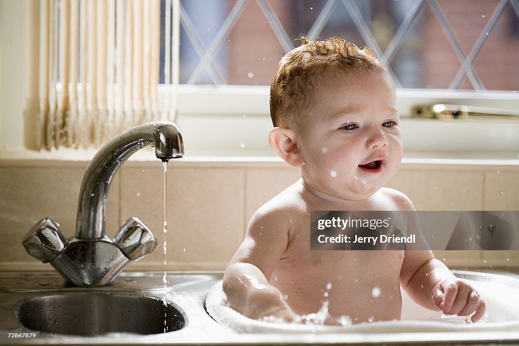 Baby girl (6-9 months) splashing water in kitchen sink, smiling