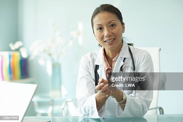 female doctor sitting at table, smiling, portrait - talking stock pictures, royalty-free photos & images