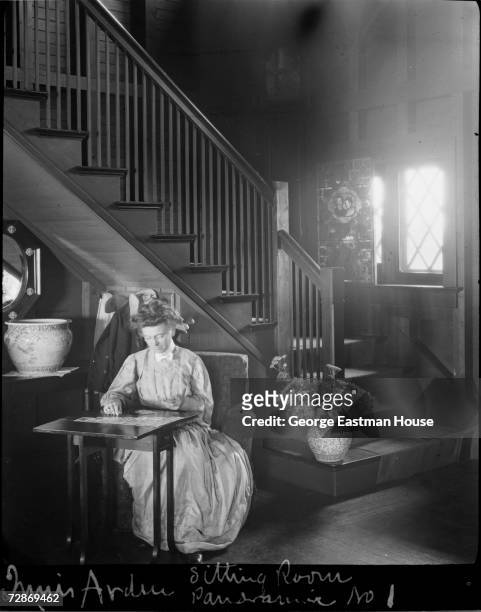 An unidentified woman plays solitaire at a folding table at the foot of a staircase in Innis Arden, Greenwich, Connecticut. 1907. The mansion was...