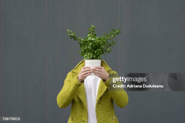 Primer plano de una persona con una planta en maceta sobre fondo gris