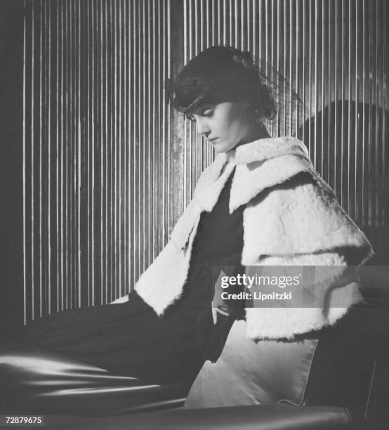 Fashion model sits on a chair and wears a hat designed by French fashion designer Jeanne Lanvin, Paris, February 1935.