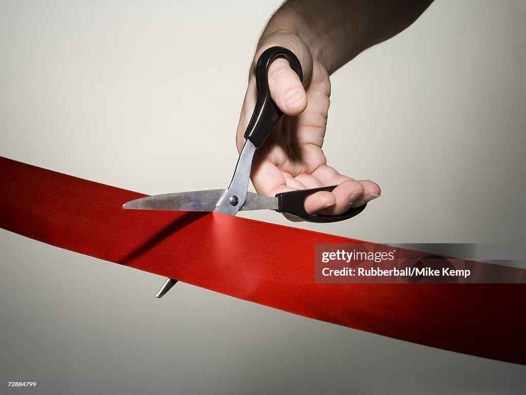 Hand cutting a red ribbon with scissors