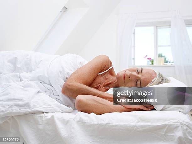 mature woman sleeping in her bed - nachtwäsche stock-fotos und bilder