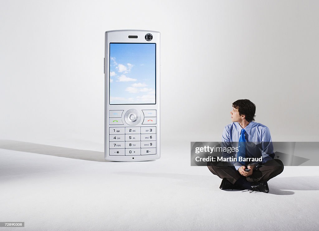 Businessman sitting beside giant model mobile phone