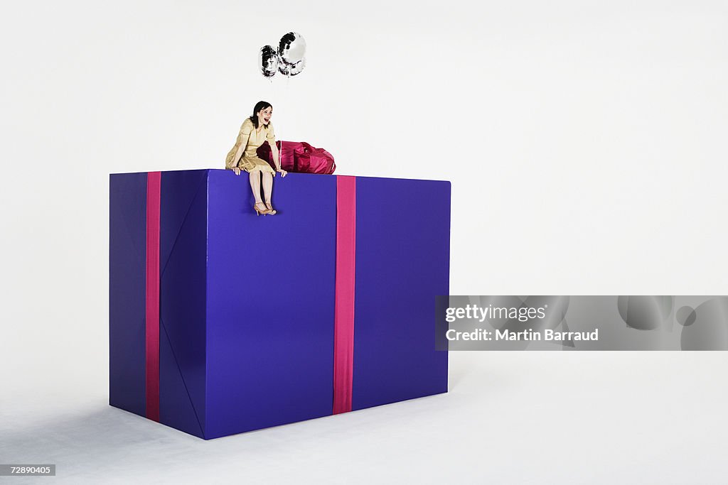Young woman sitting on edge of giant present, laughing