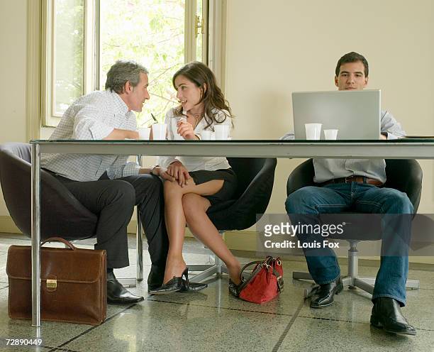 mature businessman with his hand on knee of young businesswoman under meeting room table - hand on knee ストックフォトと画像