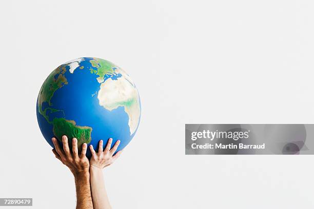 two people holding globe in raised hands against white background,close-up - people holding hands around globe stock-fotos und bilder